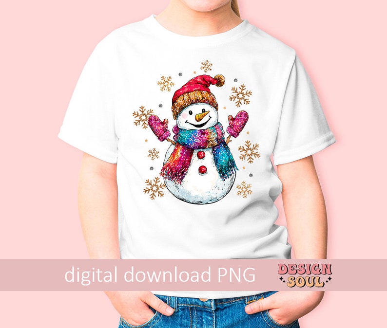 May include: A white t-shirt with a colorful snowman design. The snowman is wearing a red hat, a pink and purple scarf, and has a carrot nose. The design is surrounded by gold glitter snowflakes.
