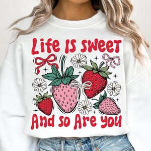 May include: White sweatshirt with a red graphic that says "Life is sweet and so are you". The graphic also features strawberries, flowers, and bows.