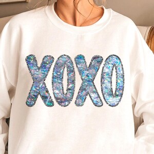 May include: White sweatshirt with a sparkly iridescent blue and silver "XOXO" graphic.