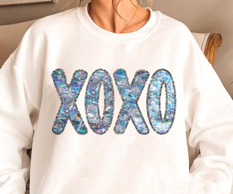 May include: White sweatshirt with a sparkly iridescent blue and silver "XOXO" graphic.
