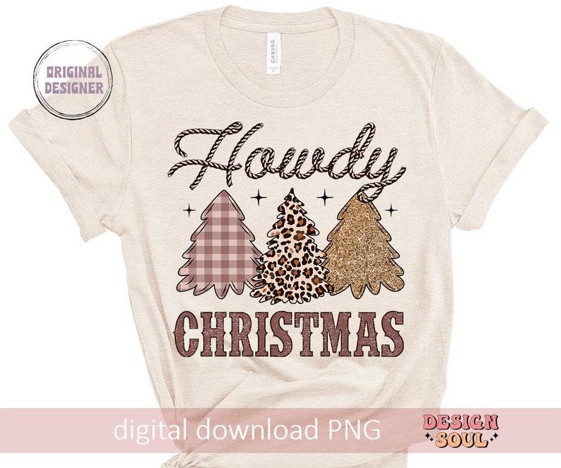May include: A beige t-shirt with the text "Howdy Christmas" in pink and brown. The text is surrounded by three stylized Christmas trees in pink, brown, and gold.