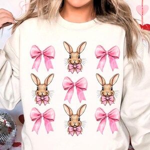 May include: White sweatshirt with a repeated pattern of brown bunnies wearing pink bows.