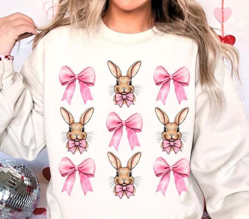 May include: White sweatshirt with a repeated pattern of brown bunnies wearing pink bows.