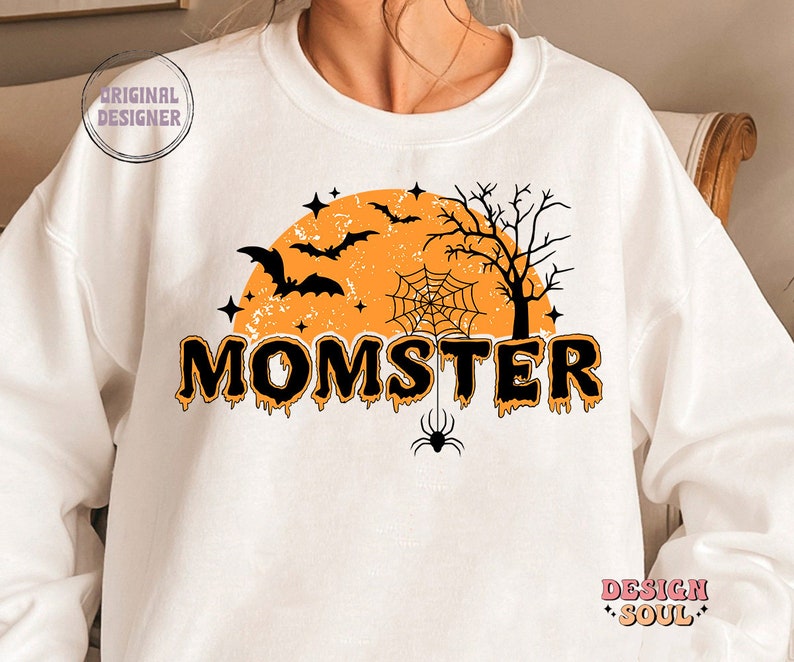 May include: White sweatshirt with a black and orange Halloween design. The design features a moon, bats, a spider web, a spider, and the text "MOMSTER".