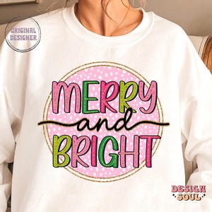 May include: White sweatshirt with a pink polka-dot circle design. The words "MERRY and BRIGHT" are in green and pink lettering, with a gold glitter outline. The words are separated by a black line. The sweatshirt has the text "ORIGINAL DESIGNER" and "DESIGN SOUL" on it.