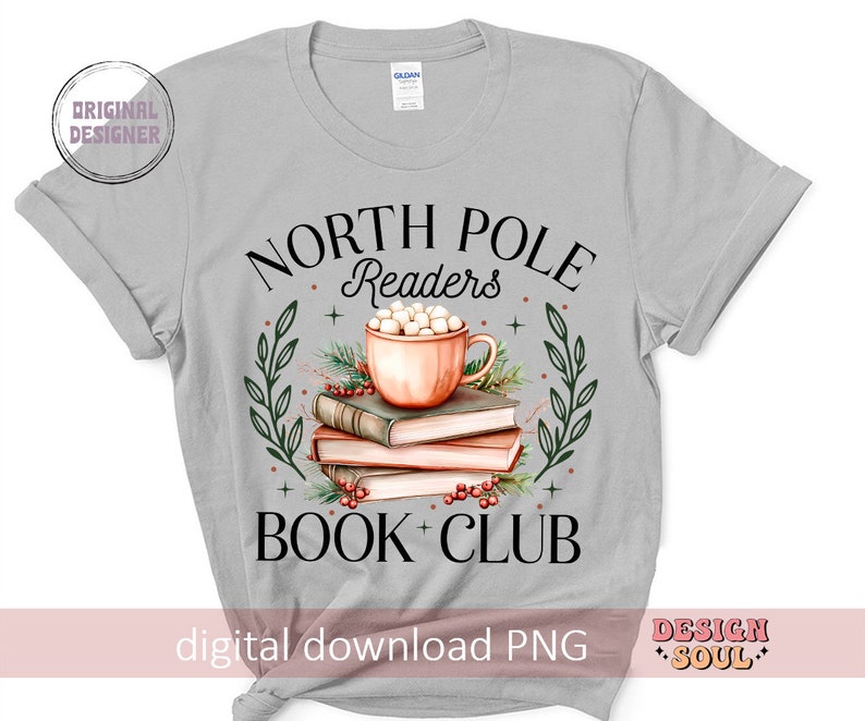 May include: A gray t-shirt with the text "North Pole Readers Book Club" in black. The design features a cup of hot chocolate with marshmallows and a stack of books.