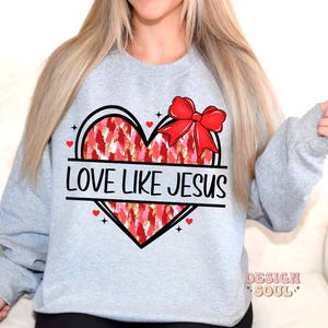 May include: Gray sweatshirt with a red heart design and the text "Love Like Jesus". The heart has a red bow and a white and red patterned design.