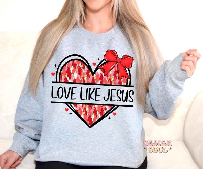 May include: Gray sweatshirt with a red heart design and the text "Love Like Jesus". The heart has a red bow and a white and red patterned design.
