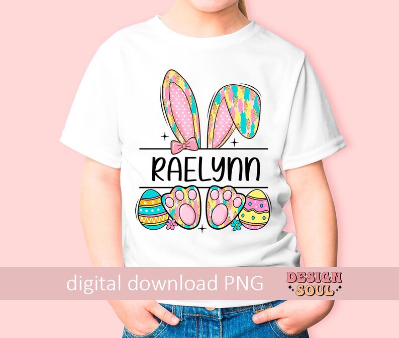 May include: White t-shirt with a pink and yellow bunny ears design, Easter egg accents, and the name "Raelynn" printed on the front.