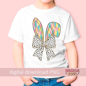 May include: A white t-shirt with a colorful bunny ear design and a black and white polka dot bow. The design features gold glitter accents.