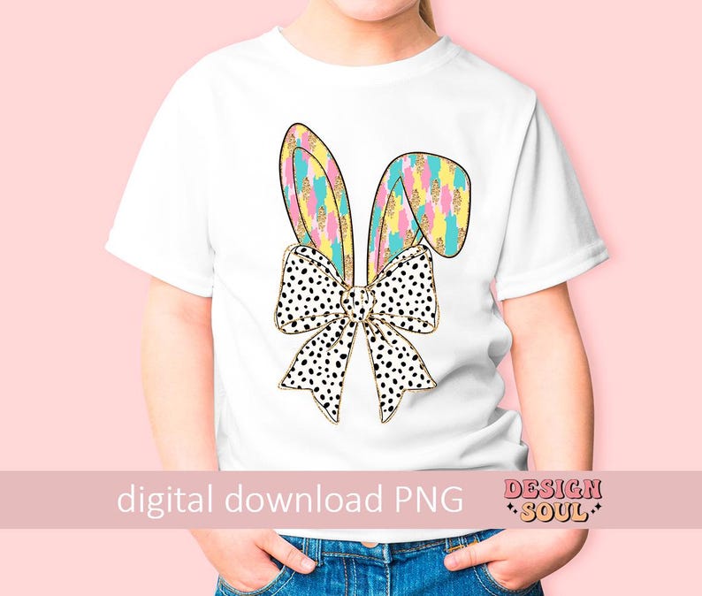 May include: A white t-shirt with a colorful bunny ear design and a black and white polka dot bow. The design features gold glitter accents.