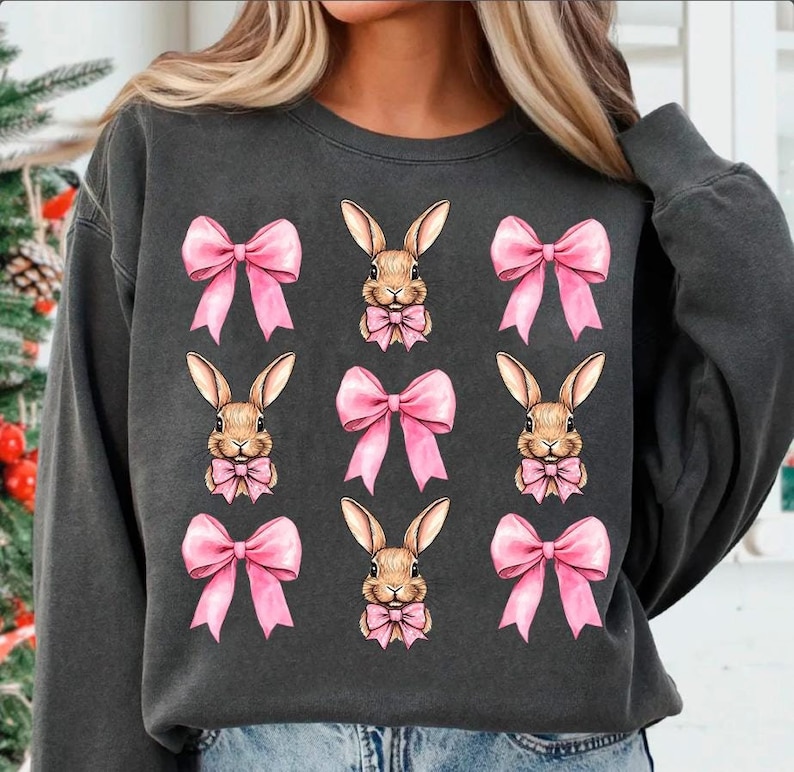 May include: A gray sweatshirt with a repeating pattern of pink bows and brown bunnies. The bunnies have pink bows around their necks.