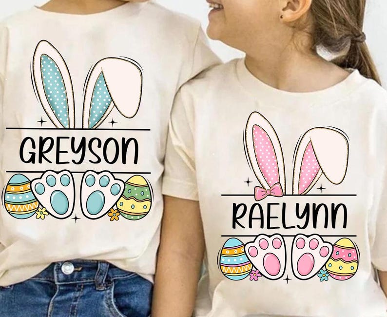 May include: Two white t-shirts with bunny ears and Easter egg designs. The shirts have the names "Greyson" and "Raelynn" printed on them.