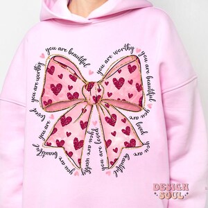 May include: Pink hoodie with a large gold bow with pink hearts and the text "you are beautiful you are worthy you are loved" repeated around the bow.