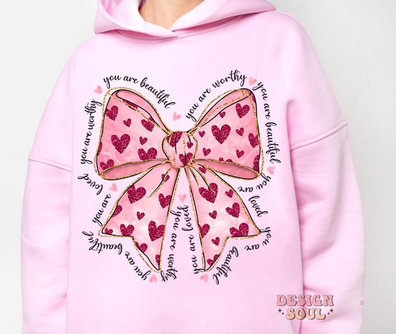 May include: Pink hoodie with a large gold bow with pink hearts and the text "you are beautiful you are worthy you are loved" repeated around the bow.