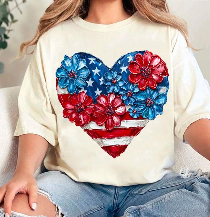 May include: A white t-shirt with a red, white, and blue heart-shaped design. The heart is made up of flowers and an American flag.