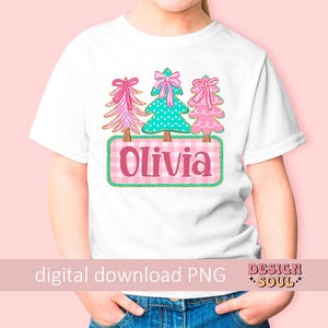 May include: White t-shirt featuring three Christmas trees with bows, a teal polka-dot tree, and a pink gingham nameplate that says "Olivia". The shirt has a pink background and the words "digital download PNG".