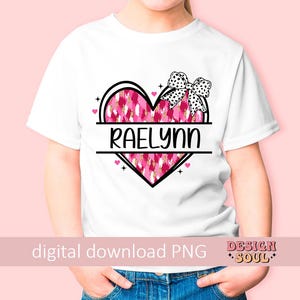 May include: White t-shirt with a pink and white heart design and the name "Raelynn" printed on it. The heart has a black outline and a black bow on top.