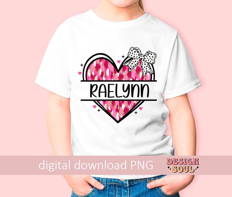 May include: White t-shirt with a pink and white heart design and the name "Raelynn" printed on it. The heart has a black outline and a black bow on top.