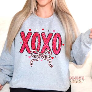 May include: A gray sweatshirt with a pink and white XOXO design with a bow and hearts. The design is made of sequins.