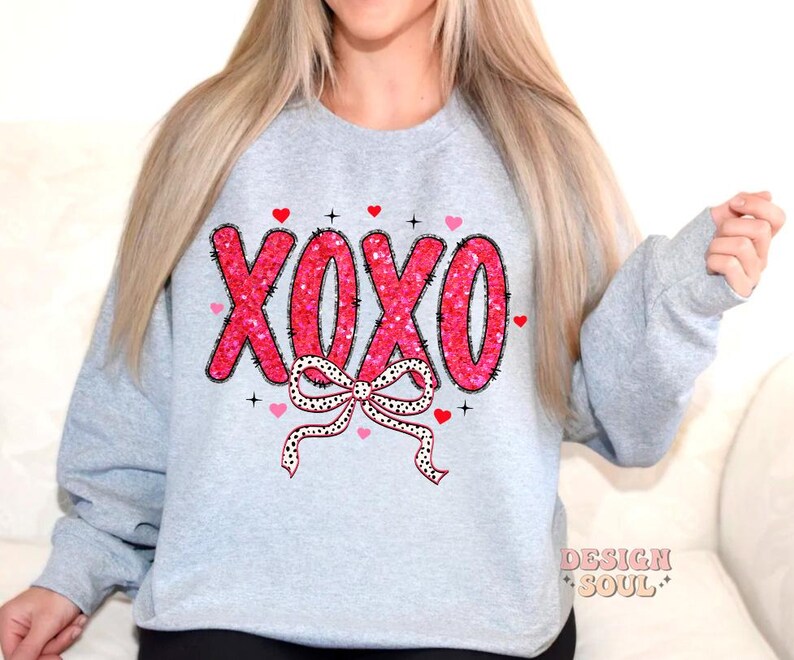 May include: A gray sweatshirt with a pink and white XOXO design with a bow and hearts. The design is made of sequins.