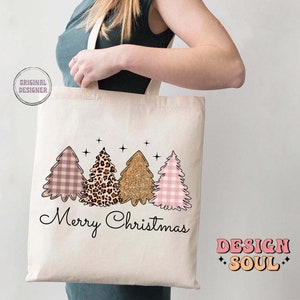 May include: A white tote bag with a pink and white gingham, leopard print, and gold glitter Christmas tree design. The text "Merry Christmas" is printed below the trees. The text "DESIGN SOUL" is printed in the bottom right corner.