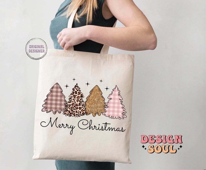 May include: A white tote bag with a pink and white gingham, leopard print, and gold glitter Christmas tree design. The text "Merry Christmas" is printed below the trees. The text "DESIGN SOUL" is printed in the bottom right corner.