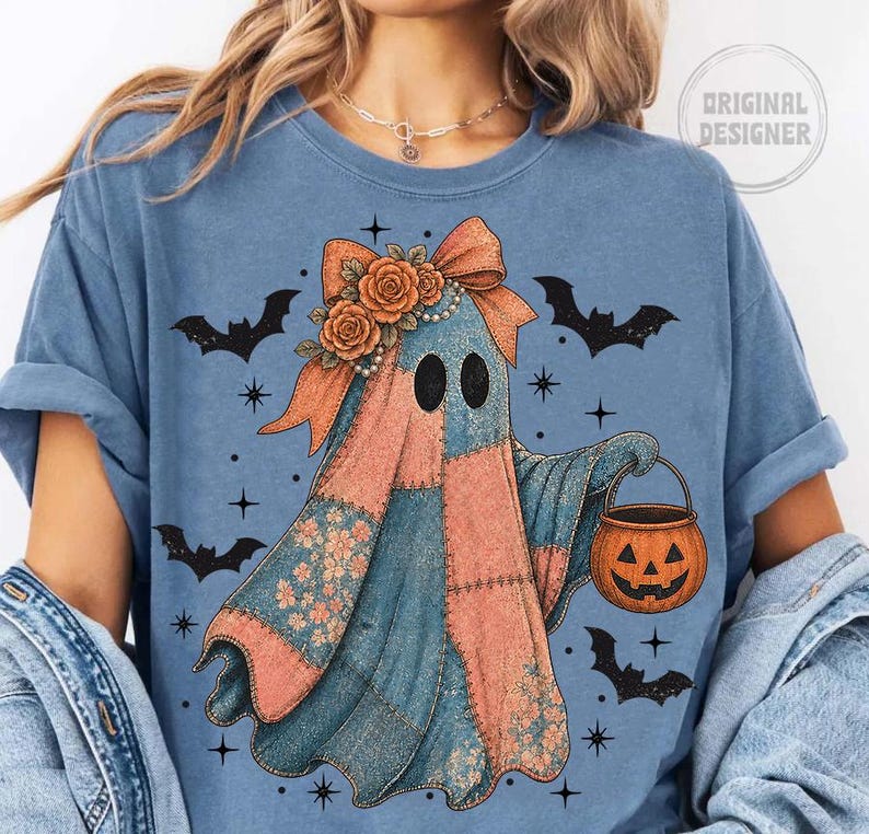 May include: A blue t-shirt featuring a patchwork ghost design with a bow, roses, and a pumpkin bucket. Black bats and stars are scattered around the ghost. The shirt has the words "Original Designer" in a circle.