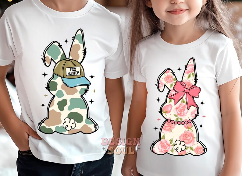 May include: Two white t-shirts with a bunny rabbit design. One bunny is camouflage with a blue and white baseball cap that says "Egg Hunter". The other bunny is pink and white with a pink bow.