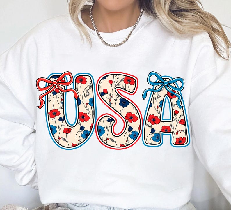 May include: White sweatshirt with a red, white, and blue floral design that spells out "USA".