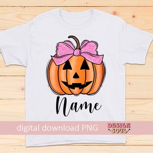 May include: A white t-shirt with a pumpkin with a pink bow on top. The pumpkin has a jack-o-lantern face. The text "Name" is below the pumpkin. The text "digital download PNG" is at the bottom left and "DESIGN SOUL" is at the bottom right.