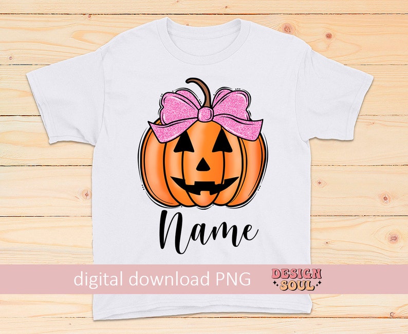 May include: A white t-shirt with a pumpkin with a pink bow on top. The pumpkin has a jack-o-lantern face. The text "Name" is below the pumpkin. The text "digital download PNG" is at the bottom left and "DESIGN SOUL" is at the bottom right.