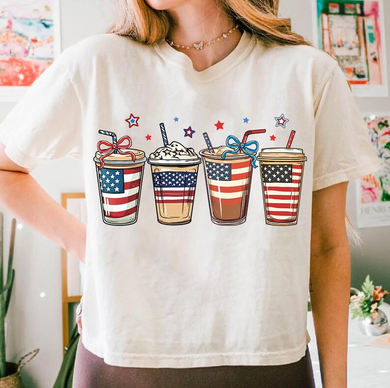 May include: White t-shirt with a graphic of four iced coffee cups decorated with the American flag.