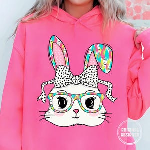 May include: Pink hoodie with a graphic of a white bunny wearing glasses and a polka dot bow. The bunny has colorful ears and a rainbow pattern on its head.