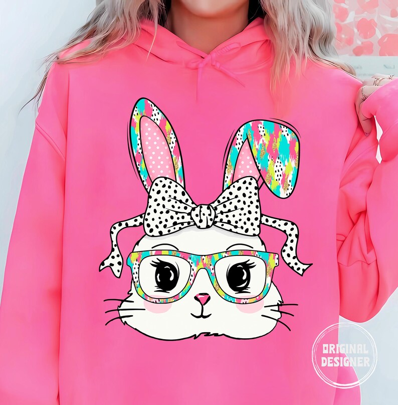 May include: Pink hoodie with a graphic of a white bunny wearing glasses and a polka dot bow. The bunny has colorful ears and a rainbow pattern on its head.