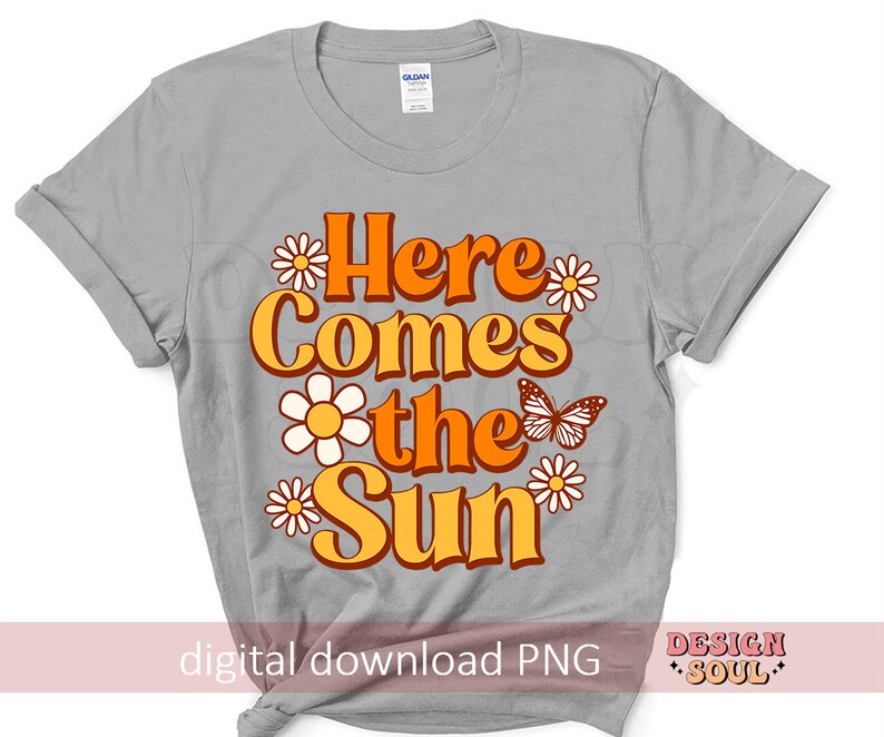 May include: A gray t-shirt with the text "Here Comes the Sun" in orange and yellow letters with a butterfly and daisies. The text is in a retro font style.