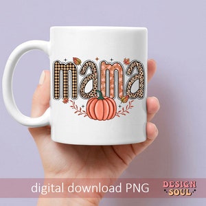 May include: White ceramic mug with a fall-themed design. The word "mama" is written in a colorful font with a pumpkin and leaves.