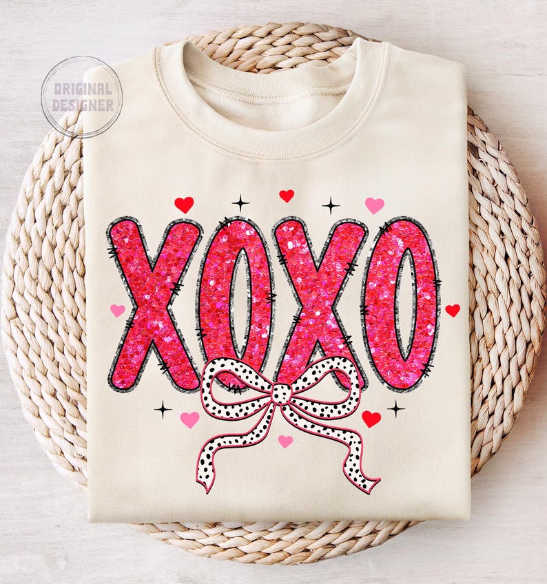 May include: A cream-colored sweatshirt with a pink sequined "XOXO" design and a black and white polka dot bow. The sweatshirt has a crew neck and long sleeves.