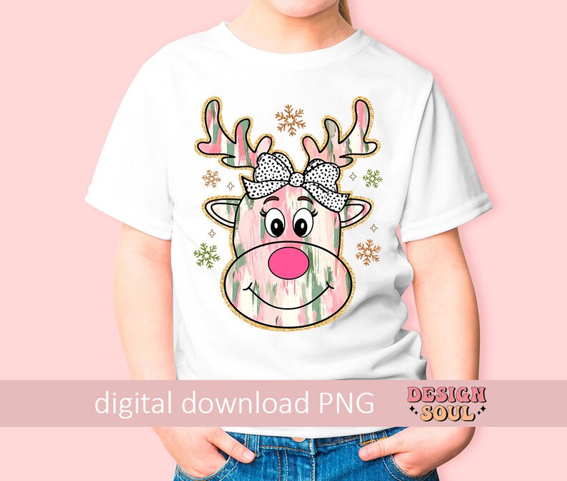 May include: A white t-shirt with a pink and green reindeer design. The reindeer has a black and white polka dot bow. The design includes gold glitter accents and snowflakes.