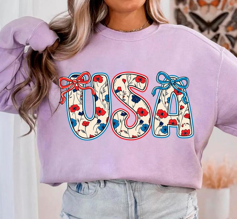 May include: A lavender sweatshirt with a floral pattern "USA" graphic. The letters are outlined in red, white, and blue.
