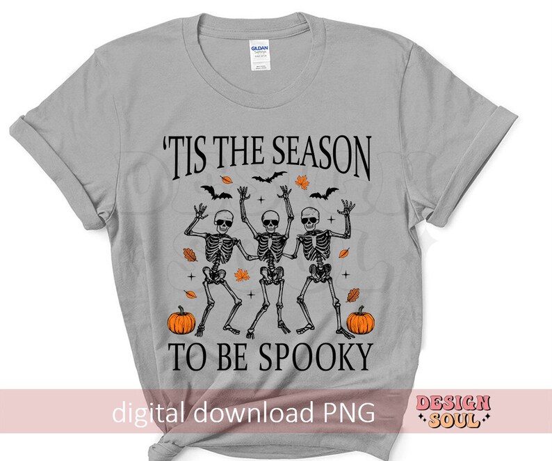 May include: A grey t-shirt with the text "'Tis the season to be spooky" in black. Three skeletons are dancing with pumpkins on either side of the text.