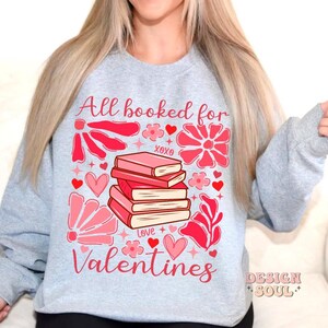 May include: Gray sweatshirt with a pink and red graphic design featuring a stack of books with the text "All booked for Valentines".
