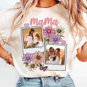 May include: Cream-colored sweatshirt with the word "Mama" in pink script. The design includes two polaroid-style photos, pink and purple flowers, a pink butterfly, and a pink heart.
