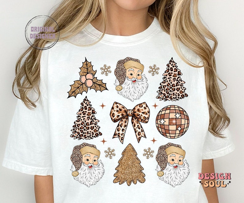 May include: White t-shirt with a festive design featuring Santa Claus, Christmas trees, a bow, a disco ball, and holly. The design is in a leopard print and gold glitter.