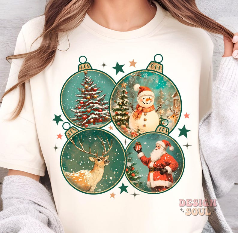 May include: A white t-shirt with a Christmas design featuring four baubles. Each bauble has a different Christmas scene: a Christmas tree, a snowman, a reindeer, and Santa Claus. The baubles are surrounded by stars and snowflakes.