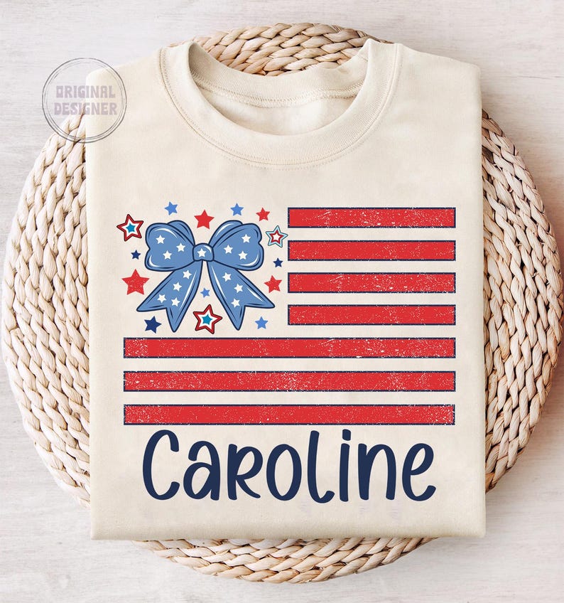 May include: A beige t-shirt with a distressed American flag design featuring a blue bow with white stars. The name "Caroline" is printed below the flag in blue.
