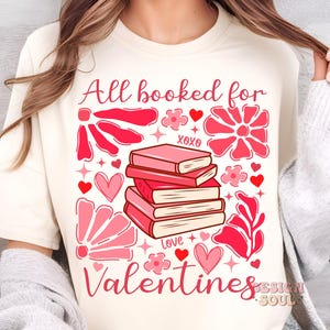 May include: A white t-shirt with the text "All booked for Valentines" in pink lettering. The design features a stack of books with pink covers, hearts, and flowers.