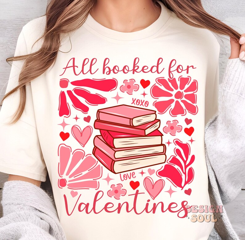 May include: A white t-shirt with the text "All booked for Valentines" in pink lettering. The design features a stack of books with pink covers, hearts, and flowers.