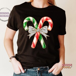 May include: Black t-shirt with a graphic of two red and green candy canes tied together with a white and black polka dot bow.