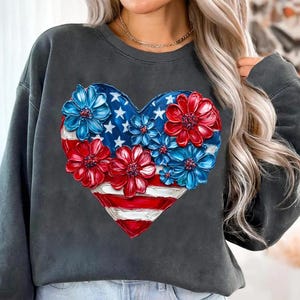 May include: A dark gray sweatshirt with a red, white, and blue heart-shaped design. The heart is made up of flowers with red, white, and blue petals. The design is reminiscent of the American flag.